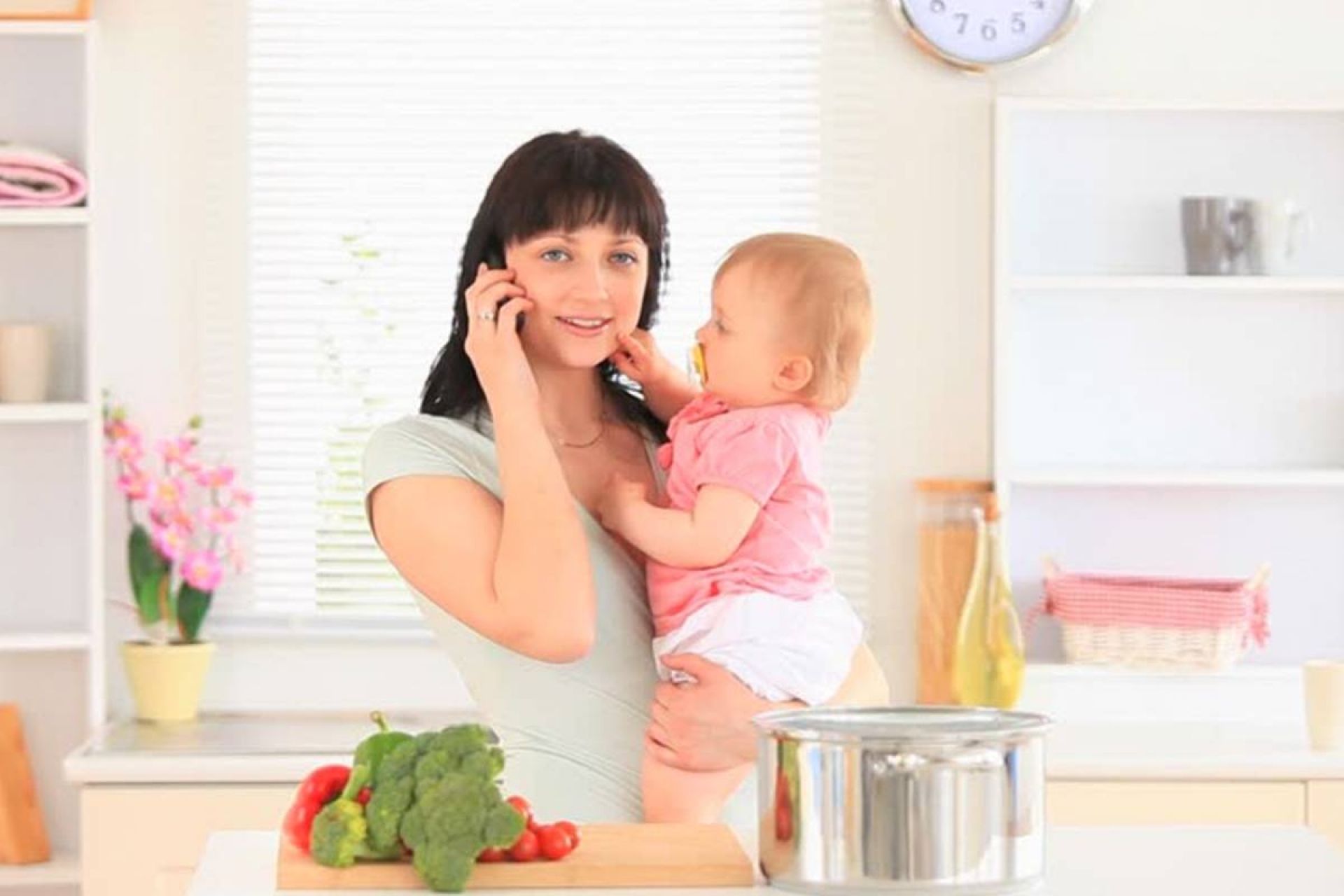 Madre multitarea: cocina, habla por teléfono mientras atiende a bebé