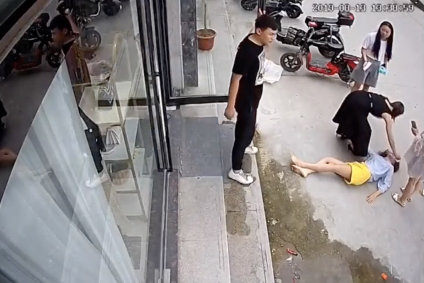 An image from surveillance footage shows Liu Zengyan on the street after jumping from a window to escape from an assault by her husband at the time, shown standing on the sidewalk, in Shangqiu, China, in August 2019. (via The New York Times)