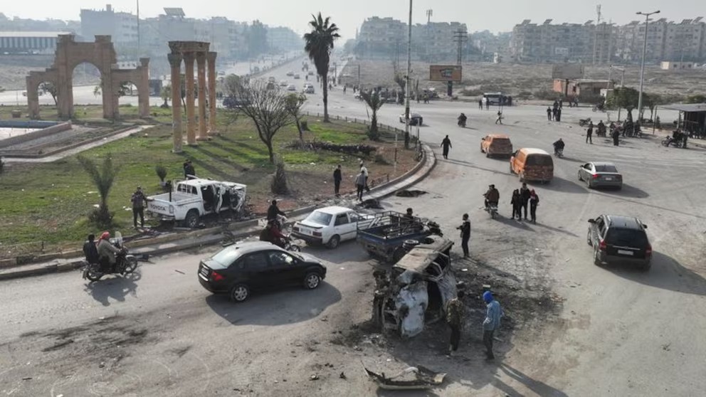 Un grupo de personas junto a un vehículo dañado, después de que los rebeldes liderados por el HTS hayan intentado aprovechar su rápida toma